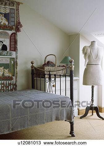 Stock Image - Dressmaker's dummy in white attic bedroom with grey bedcover on old brass bed. Fotosearch