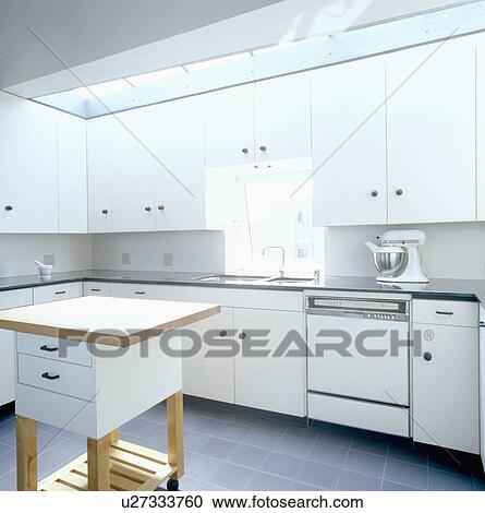 Stock Image - Electric mixer on worktop in modern white streamlined kitchen with movable island storage unit. Fotosearch