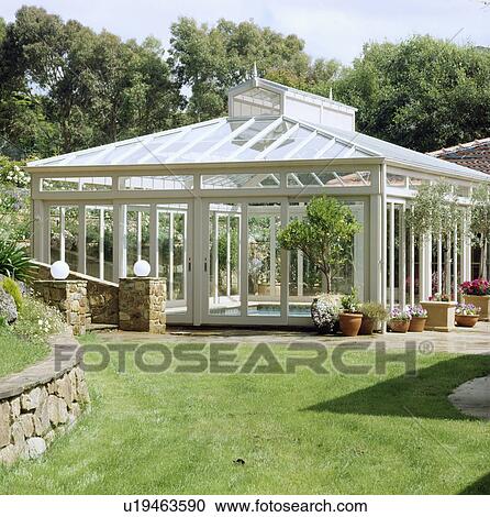 Stock Image - Exterior of glass building covering swimming pool set in garden. Fotosearch