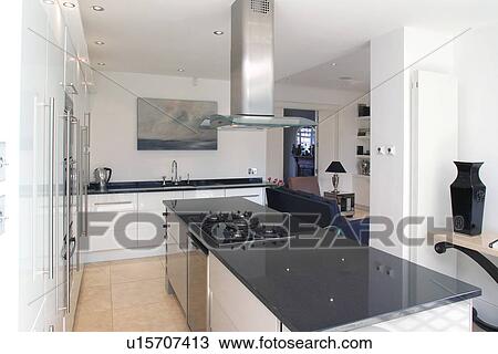 Extractor above hob set into island unit with granite worktop in modern white openplan kitchen and living room View Large Photo Image Stock Image - Extractor above hob set into island unit with granite worktop in modern white openplan kitchen and living room. Fotosearch