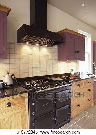 Extractor with recessed lighting and white wall tiles above black Aga in modern kitchen with wooden fitted cupboards View Large Photo Image Stock Photography - Extractor with recessed lighting and white wall tiles above black Aga in modern kitchen with wooden fitted cupboards. Fotosearch