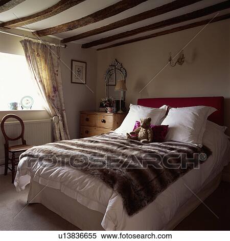 Faux fur rug and cream pillows and bedlinen on bed in cottage bedroom with beamed ceiling View Large Photo Image Stock Photography - Faux fur rug and cream pillows and bedlinen on bed in cottage bedroom with beamed ceiling. Fotosearch