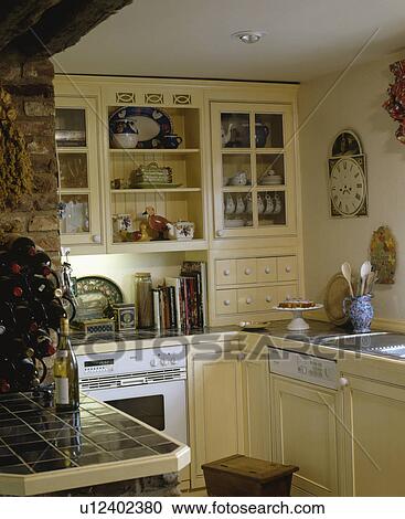 Stock Image - Fitted dishwasher and white oven in small yellow cottage kitchen with green tiled worktops. Fotosearch
