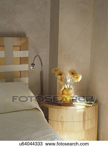 Flexible lamp and yellow gerberas in vase on pale wood table beside bed with webbing and wood headboard View Large Photo Image Stock Image - Flexible lamp and yellow gerberas in vase on pale wood table beside bed with webbing and wood headboard. Fotosearch