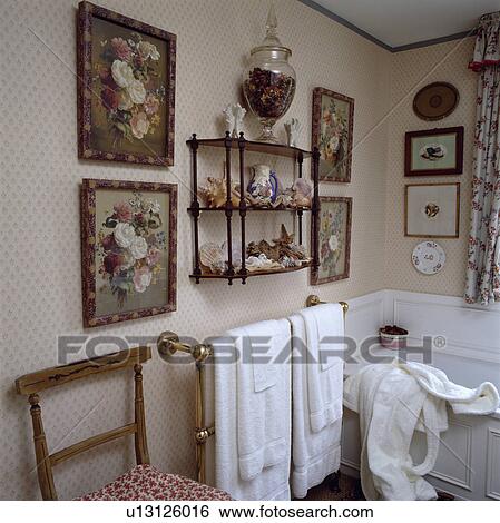 Stock Photograph - Floral pictures on either side of 3-tier Victorian wall shelf in traditional bathroom with towels on brass towel rail. Fotosearch