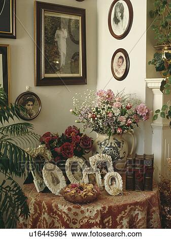 Framed photographs and fresh flowers on patterned cloth on table in corner of living room View Large Photo Image Picture - Framed photographs and fresh flowers on patterned cloth on table in corner of living room. Fotosearch