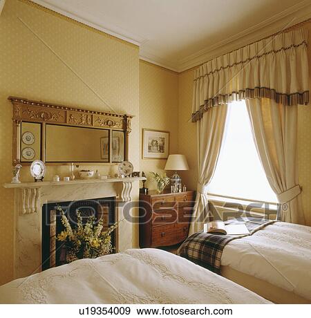 Georgian style mirror above fireplace in bedroom with twin beds and fringed pelmet on cream curtains View Large Photo Image Stock Photo - Georgian style mirror above fireplace in bedroom with twin beds and fringed pelmet on cream curtains. Fotosearch