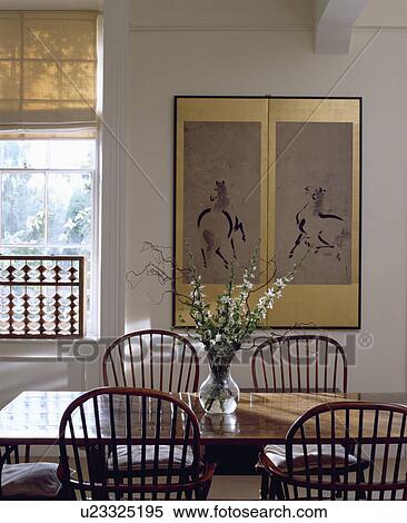 Gilt framed Chinese drawing on wall of white dining room with simple wood table and Windsor chairs View Large Photo Image Stock Photography - Gilt framed Chinese drawing on wall of white dining room with simple wood table and Windsor chairs. Fotosearch