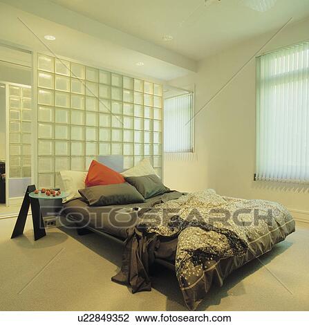 Glass brick wall behind bed with black sheets and patterned monochrome duvet in modern white bedroom View Large Photo Image Stock Image - Glass brick wall behind bed with black sheets and patterned monochrome duvet in modern white bedroom. Fotosearch