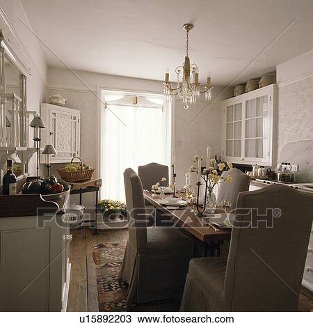 Glass chandelier above rectangular wooden table and chairs with loosecover in white country dining room View Large Photo Image Stock Image - Glass chandelier above rectangular wooden table and chairs with loosecover in white country dining room. Fotosearch