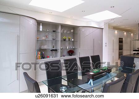 Glass table and upholstered black chairs in modern openplan white kitchen and dining room with fitted shelving unit View Large Photo Image Stock Image - Glass table and upholstered black chairs in modern openplan white kitchen and dining room with fitted shelving unit. Fotosearch