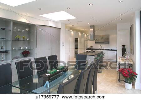 Stock Photo - Glass table and upholstered black chairs in modern openplan white kitchen and dining room. Fotosearch