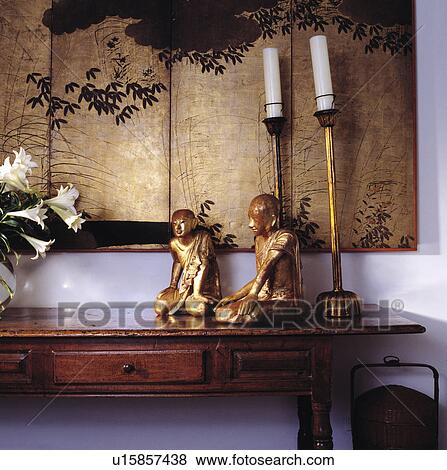 Stock Photo - Gold Asian statues and tall candlesticks on table below gilded oriental picture. Fotosearch