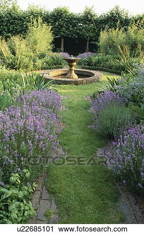 Stock Image - Grass path leading through scented herbs to circular pond in country garden. Fotosearch