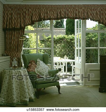 Stock Photo - Green armchair in front of French windows with patterned curtains. Fotosearch
