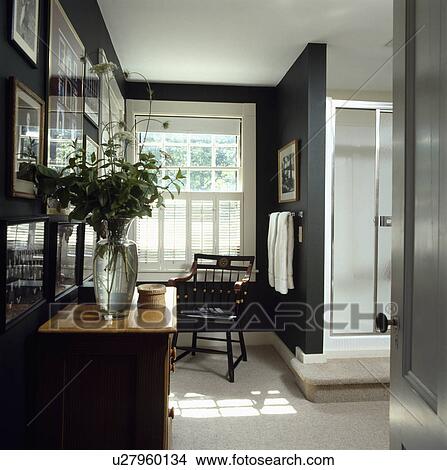 Picture - Green leaves in glass vase on chest of drawers in modern black+white bathroom with white plantation shutters. Fotosearch