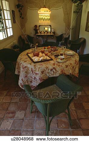 Green Lloyd Loom chair beside circular table with floral cloth and place settings in dining room with beaded lampshade View Large Photo Image Stock Photo - Green Lloyd Loom chair beside circular table with floral cloth and place settings in dining room with beaded lampshade. Fotosearch