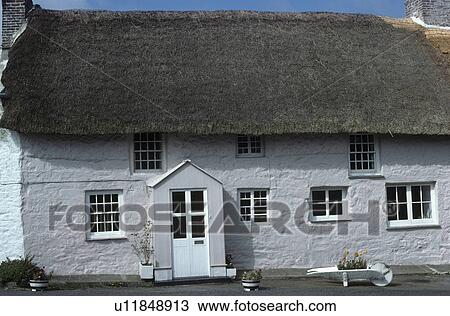 Stock Image - Grey cottage with thatched roof. Fotosearch