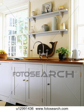 Grey Shelves On Cream Wall Of Modern Kitchen With Pale Grey Fitted Cupboards Stock Photograph