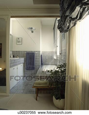 Stock Photography - Grey silk ruched blind and cream sheer curtains on landing with open doorway to grey tiled bathroom. Fotosearch