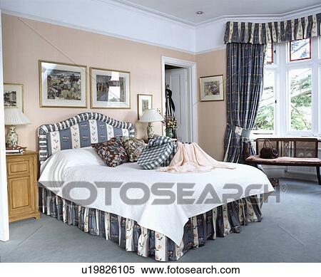 Stock Photography - Grey striped and floral upholstered bed and vallance and matching curtains in traditional bedroom with grey carpet. Fotosearch
