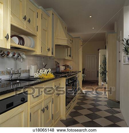 Stock Photo - Grey+white chequerboard floor in narrow kitchen with painted cream fitted cupbaords . Fotosearch