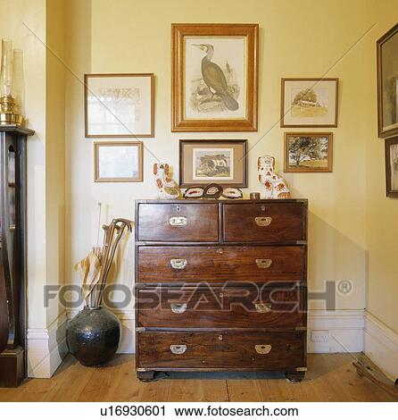 Stock Image - Group of pictures on wall above antique chest of drawers. Fotosearch