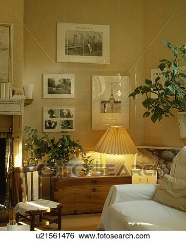 Stock Photograph - Group of pictures on wall above lighted lamp on wooden chest in traditional living room. Fotosearch