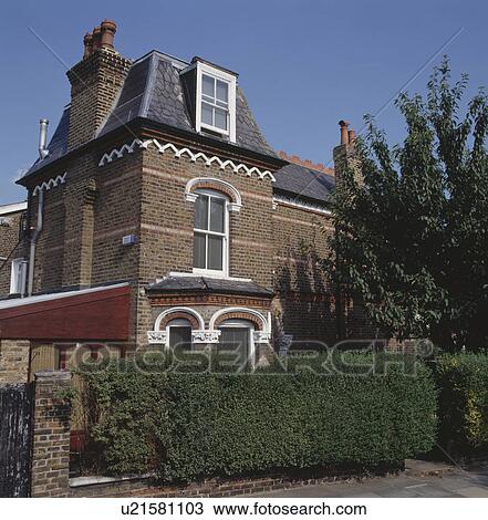 Stock Image - Hedge in front of large Victorian townhouse with mansard window. Fotosearch