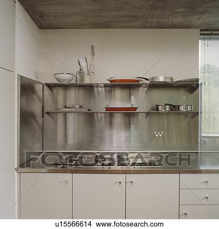 Picture - Hob set into stainless steel worktop below shelves and stainless steel splashback in modern white kitchen. Fotosearch