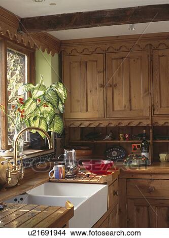 Picture - Houseplant on windowsill above white ceramic double sink in fitted wooden country kitchen. Fotosearch
