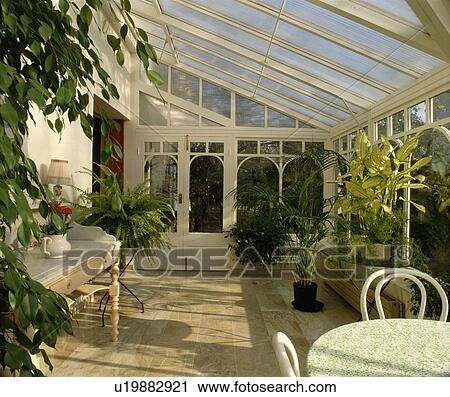 Stock Image - Houseplants in glass conservatory dining room with marble floor. Fotosearch
