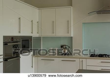 Stock Photo - Kettle on worktop in modern white kitchen with turquoise wall below cupboards. Fotosearch