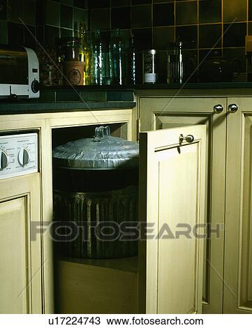 Stock Image - Kitchen cupboard door open to show galvanised wastebin. Fotosearch