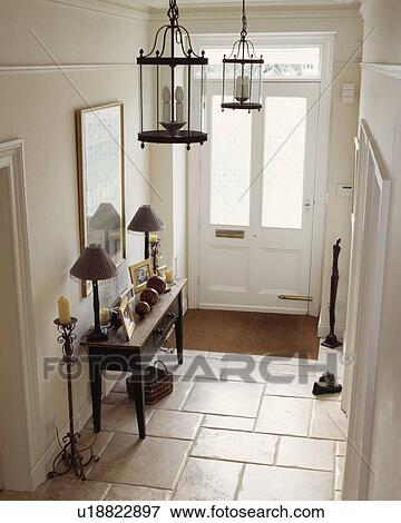 Stock Photo - Lamps on antique wooden console table in white hall with white tiled floor and large glass lanterns. Fotosearch