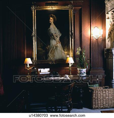 Stock Image - Large Edwardian portrait above table with lighted lamps in panelled study. Fotosearch