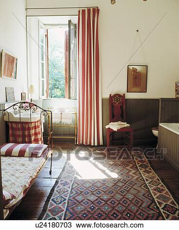 Stock Image - Large traditional bathroom with high ceilings, dark wood panelling around bath and day bed.. Fotosearch