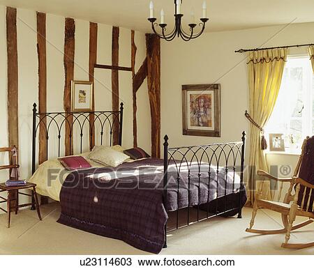 Stock Image - Large traditional bedrooms with rocking chair and iron framed bed against white painted wall with breams. Fotosearch