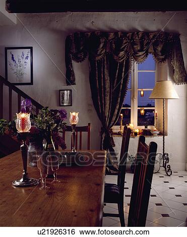 Lighted candles in glass and wood candlesticks on wooden table in eighties dining room with swagged and tailed curtain View Large Photo Image Stock Photograph - Lighted candles in glass and wood candlesticks on wooden table in eighties dining room with swagged and tailed curtain. Fotosearch
