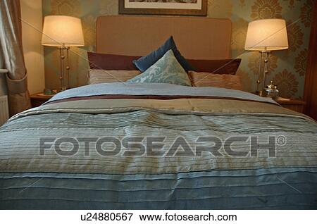 Lighted lamps on either side of bed with striped duvet in modern bedroom View Large Photo Image Stock Photo - Lighted lamps on either side of bed with striped duvet in modern bedroom. Fotosearch