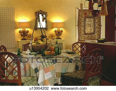 Stock Image - Lighted lamps on shelf in dining room with patchwork cloth on table. Fotosearch