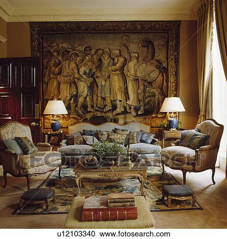 Stock Image - Lighted lamps on tables in traditional living room with large tapestry on wall. Fotosearch