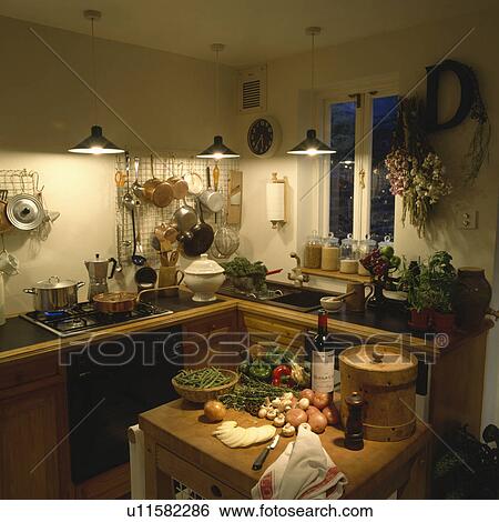 Lighted pendant lamps in small kitchen with fitted wooden cupboards butcher's block with food preparation View Large Photo Image Stock Photograph - Lighted pendant lamps in small kitchen with fitted wooden cupboards butcher's block with food preparation. Fotosearch