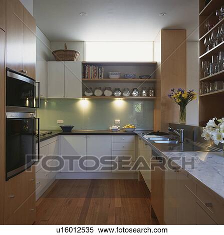 Stock Photography - Lighting above worktop in modern white kitchen with wooden flooring . Fotosearch
