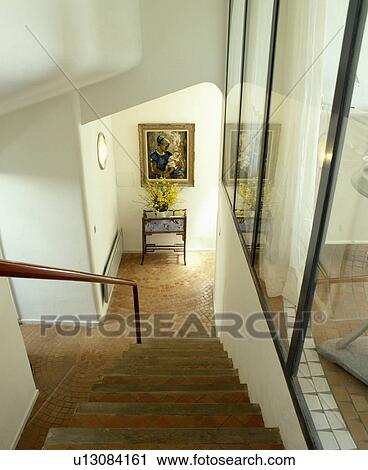 Stock Image - Looking down staircase with terracotta tiles to white hall with patterned terracotta tiled floor. Fotosearch