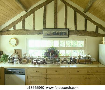 Stock Image - Low apex ceiling above wooden fitted cupboards in country kitchen. Fotosearch