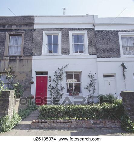 Picture - Low hedge on wall in front of terraced white Victorian townhouse with red front door. Fotosearch