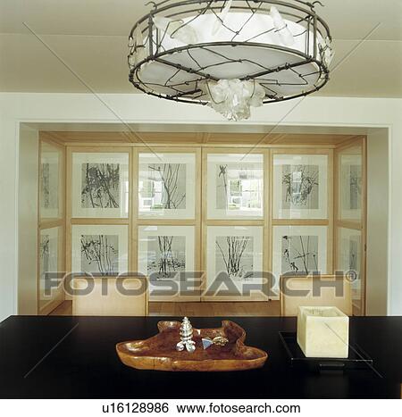 Metal and glass cylindrical light above table in modern dining room with collection of framed black+white prints on wall View Large Photo Image Stock Photograph - Metal and glass cylindrical light above table in modern dining room with collection of framed black+white prints on wall. Fotosearch