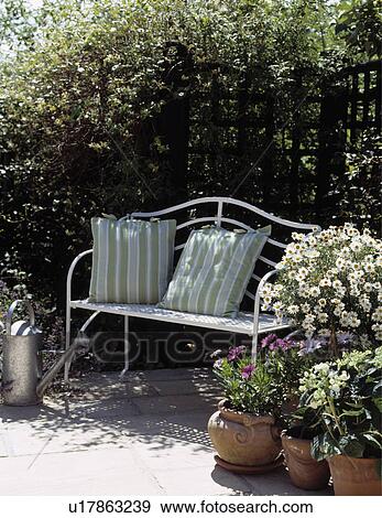 Stock Photo - Metal bench on patio with flowering plants in pots. Fotosearch