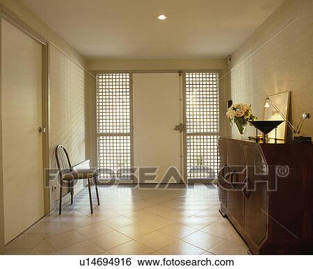 Metal chair and Thirties wood sideboard in modern white hall with white tiled floor and door between mesh windows View Large Photo Image Stock Photograph - Metal chair and Thirties wood sideboard in modern white hall with white tiled floor and door between mesh windows. Fotosearch